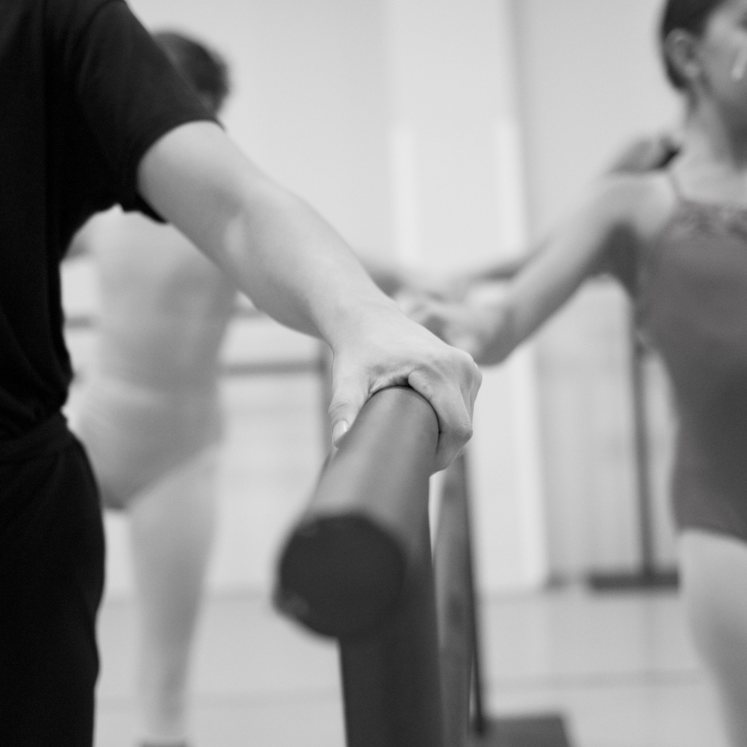 Adult ballet students practicing at the barre during class, focusing on posture and alignment.