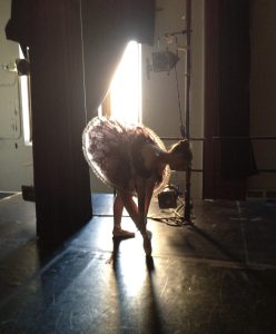 Ballet student adjusting pointe shoes backstage before performance
