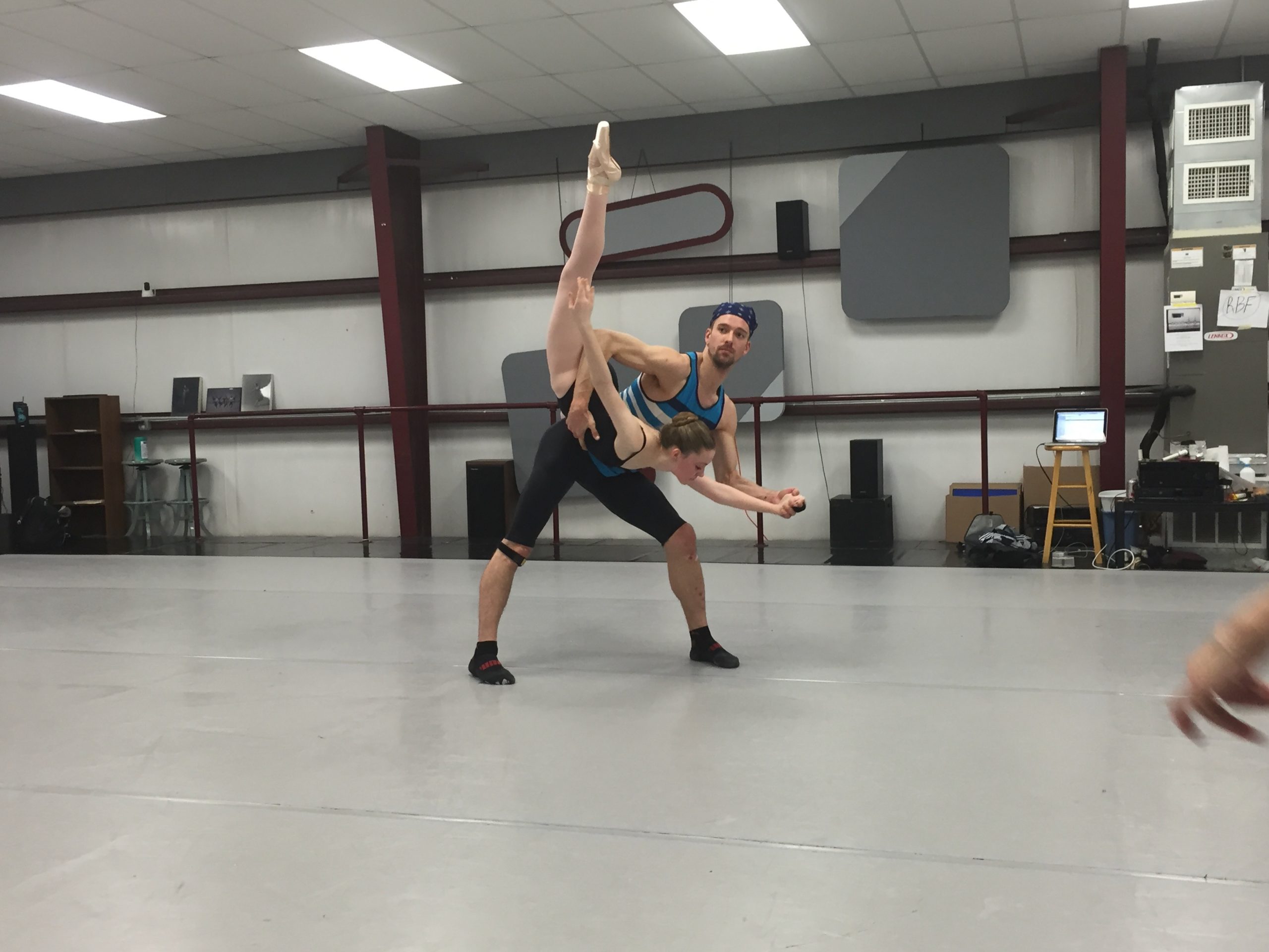 Two young ballet dancers perform a partnered pose in the studio — the male dancer supports his partner’s arabesque with graceful confidence and precision.