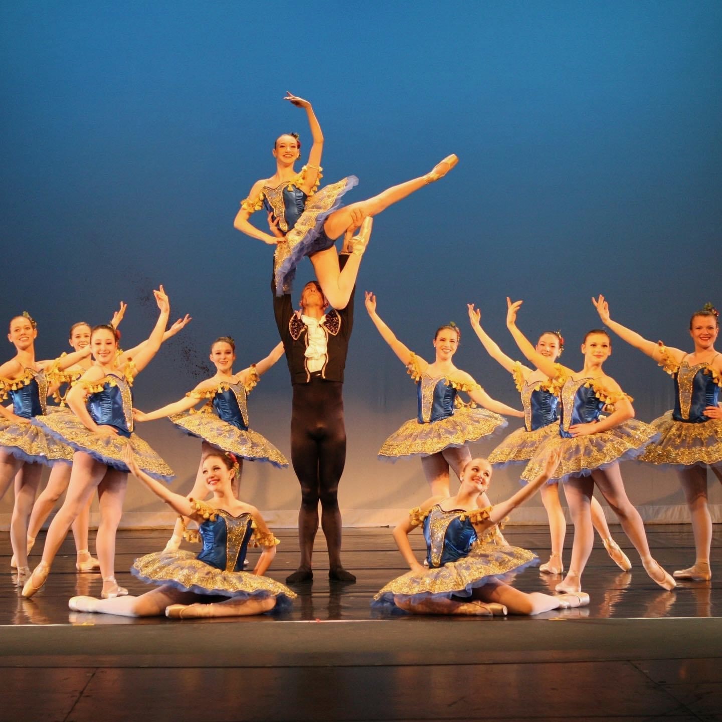 An adult male dancer performs a dramatic partnered lift in the studio, supporting his partner’s extended leg in a modern ballet pose that showcases both athletic strength and artistic balance.